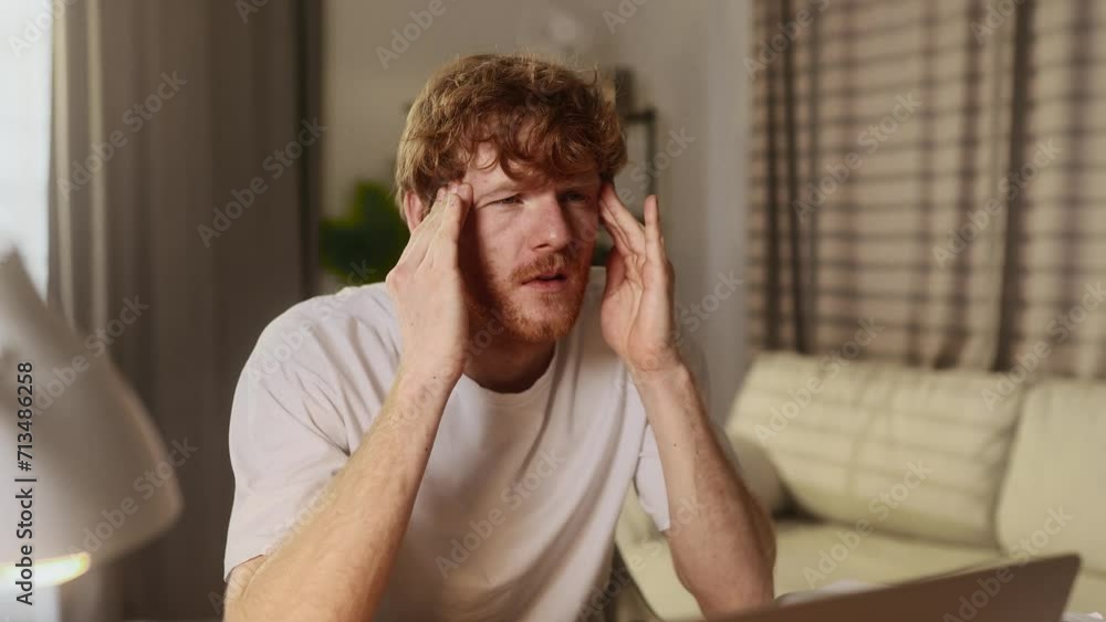 Unhappy young man student or freelancer with closing eyes suffering headache painful feelings chronic migraine high or low pressure after hard laptop computer work at home workplace Unhappy young man student or freelancer with closing eyes suffering headache painful feelings chronic migraine high or low pressure after hard laptop computer work at home workplace