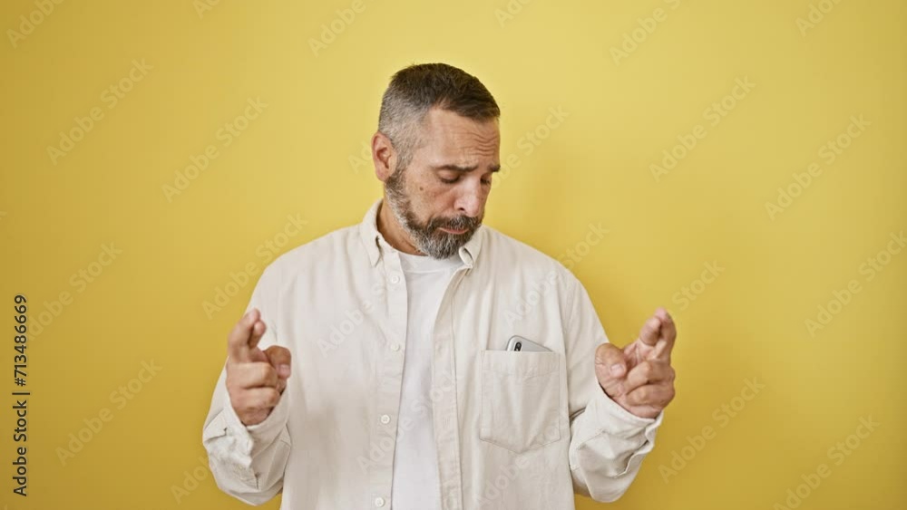 Mature bearded man crossing fingers, talking on phone, and celebrating against a yellow wall. Mature bearded man crossing fingers, talking on phone, and celebrating against a yellow wall.