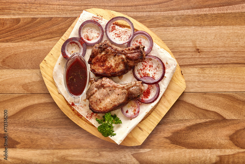 Fried beef meat with red onion rings, sauce and pita bread on the wooden board on the wooden table, flat lay top view