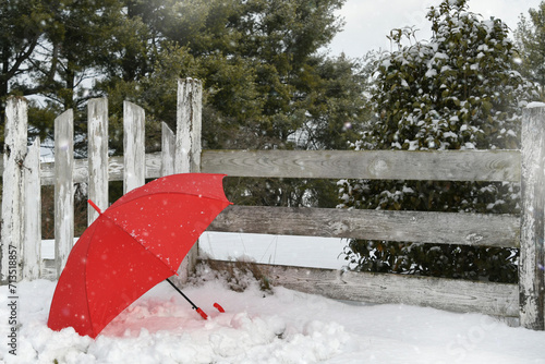 Fototapeta Naklejka Na Ścianę i Meble -  Red umbrella in the snow next to an old wooden fence and gate - winter weather concept background