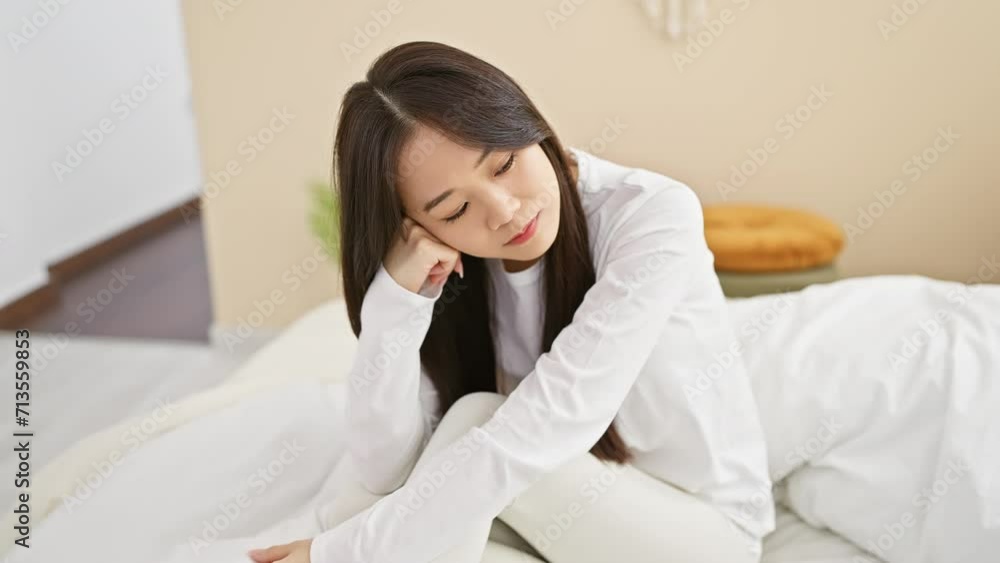 Portrait of a contemplative young asian woman sitting thoughtfully in her bedroom in a modern apartment. Portrait of a contemplative young asian woman sitting thoughtfully in her bedroom in a modern apartment.