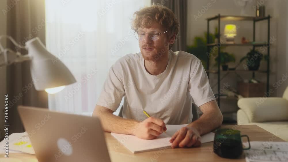 Handsome focused young man preparing for exam at university studying at home workplace Busy student make notes while looking at laptop computer screen and looking at camera Distance remote education Handsome focused young man preparing for exam at university studying at home workplace Busy student make notes while looking at laptop computer screen and looking at camera Distance remote education