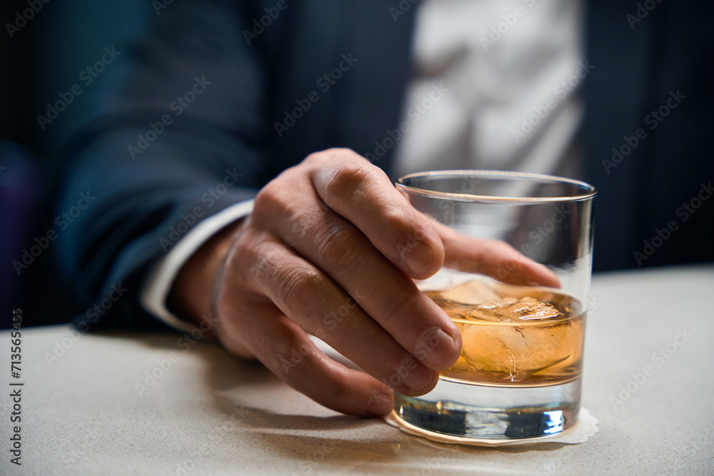 Close up of glass cup with cognac or whiskey in hands of blurred businessman Close up of glass cup with cognac or whiskey in hands of blurred businessman