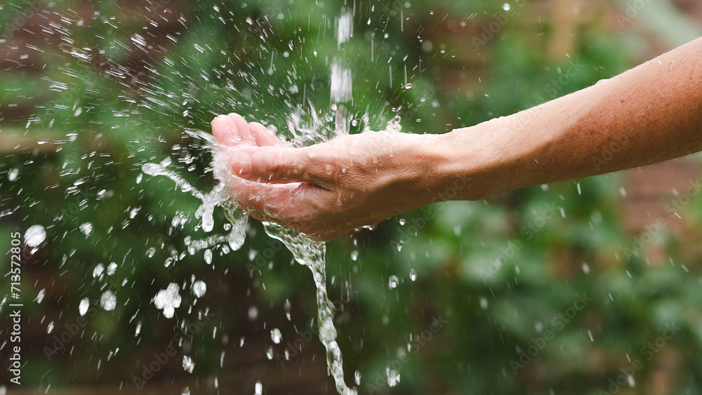 Fototapeta premium Woman's hand splashing water in the garden. Close up.