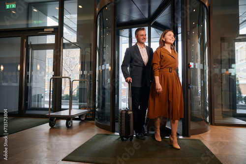 Adult caucasian couple with suitcases entering to hotel lobby at sunny day