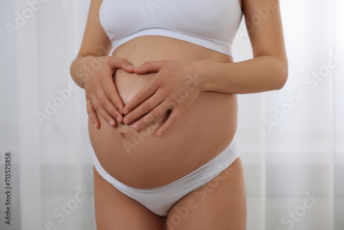 Pregnant woman in stylish comfortable underwear making heart with hands on her belly indoors, closeup © New Africa