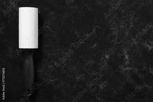 Lint roller and pet hair on black fabric, top view. Space for text photo