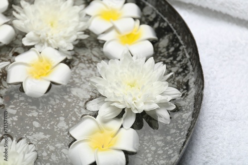Bowl of water with flowers and towel on table, closeup. Spa treatment