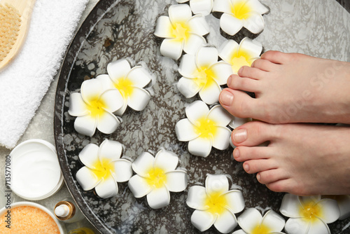 Woman soaking her feet in bowl with water and flowers on floor, top view. Spa treatment