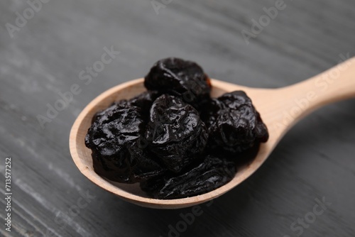 Sweet dried prunes in spoon on grey wooden table, closeup