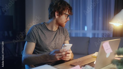 Nervous stressed young man freelancer typing quickly on laptop hurry up scream and warning about deadline while having paper and computer work at late night at home workplace photo