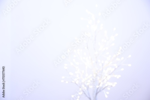 Decorative tree with lights on light background, blurred view. Space for text