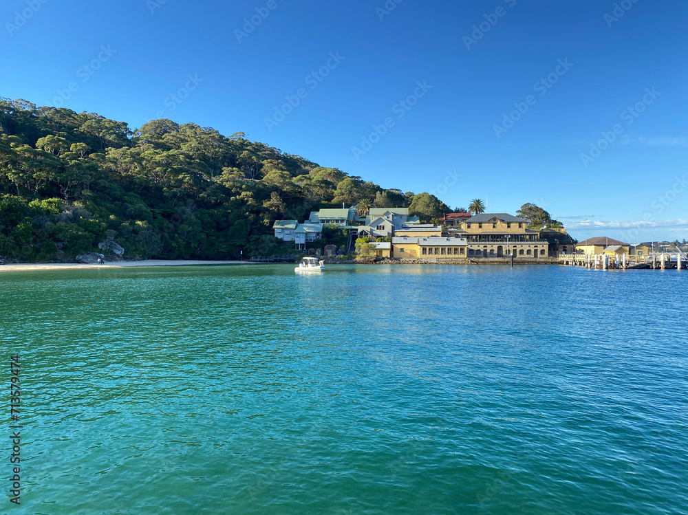Tropical island in the sea. Panoramic view of a paradisiacal coastal village from the turquoise ocean. Cluster of buildings on the island's coastline near a harbor. Sydney, Australia.