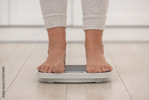 Menopause, weight gain. Woman standing on floor scales indoors, closeup