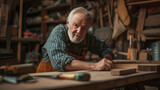 Elderly carpenter with a friendly smile standing in his well-organized woodworking workshop, full of tools and timber.