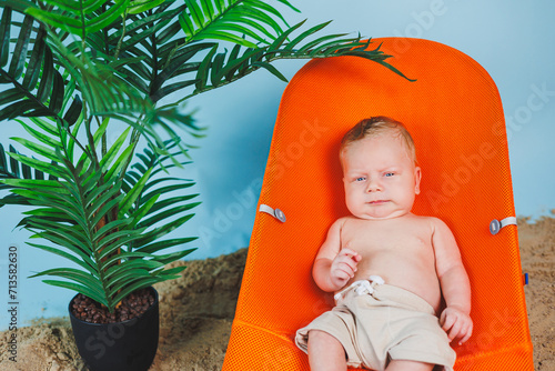 A small newborn baby is lying on an orange lounger. A child in a chair sits on the sand. The concept of summer vacation.