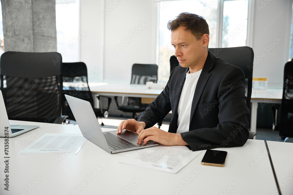 Serious man in business suit sitting at workplace and typing on laptop Serious man in business suit sitting at workplace and typing on laptop
