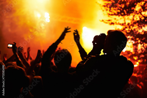 People, silhouette and camera with crowd at festival, music or concert for pictures, social media or news article. Dark, photographer or person with bright, orange and lighting for rock performance