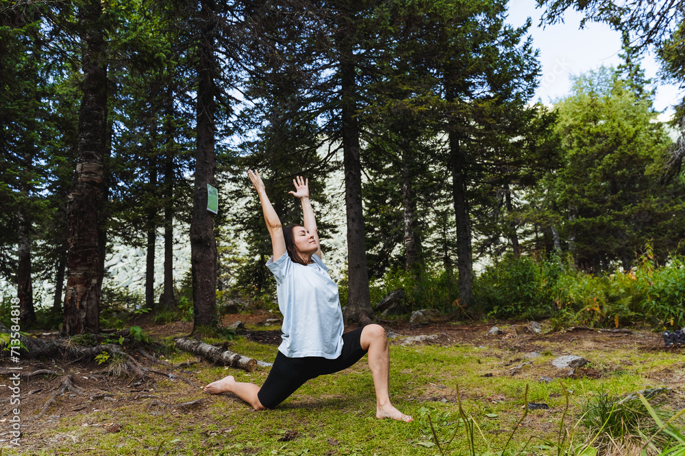 Yoga in nature in the forest, cute young girl exercising outdoors, leg stretching exercise, body bend back, balance asana.