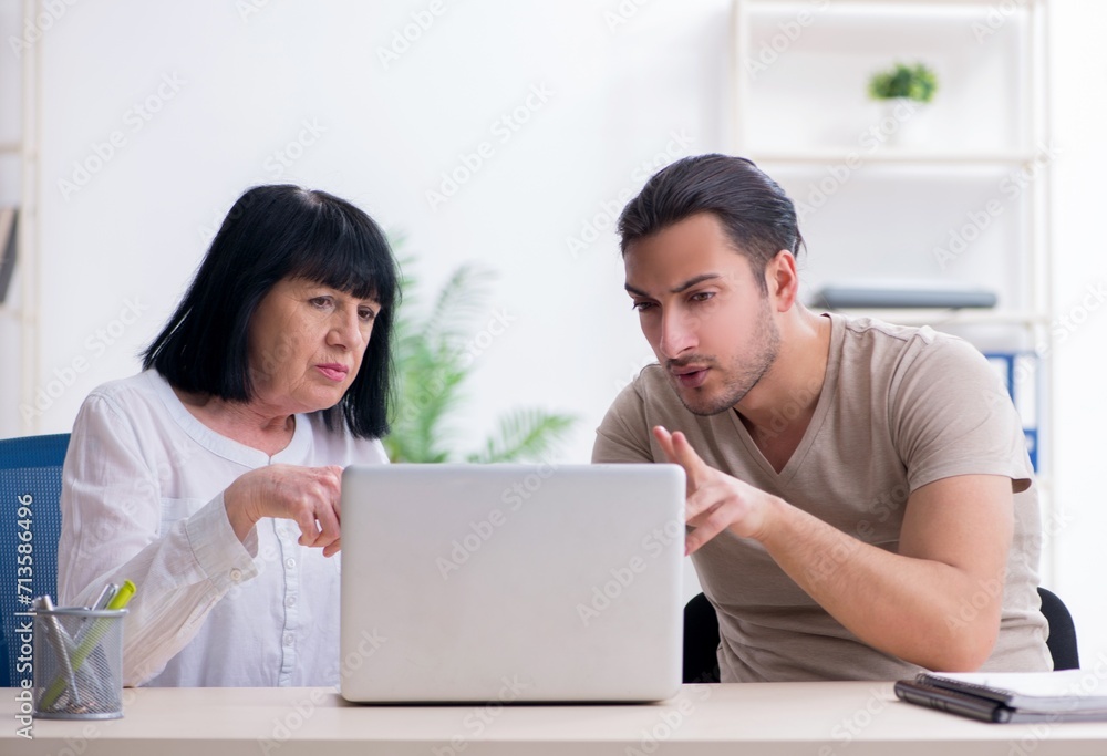 Young male employee explaining to old female colleague how to us Young male employee explaining to old female colleague how to us