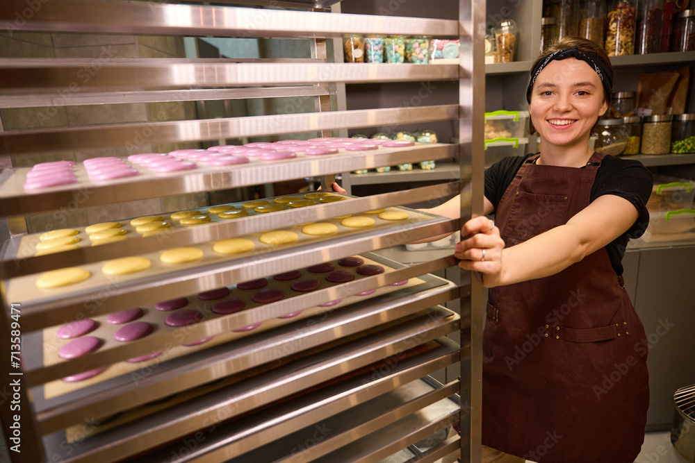Joyous pastry chef posing for camera with batch of biscuits Joyous pastry chef posing for camera with batch of biscuits