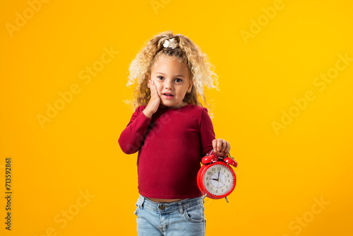 Young girl holding an alarm clock, symbolizing time management, education, school, and the urgency of deadlines and study."