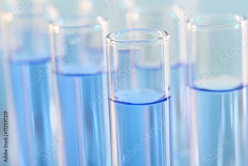 Laboratory analysis. Many glass test tubes with light blue liquid on blurred background, closeup