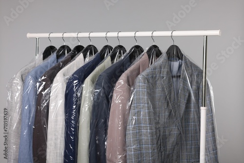 Dry-cleaning service. Many different clothes in plastic bags hanging on rack against grey background photo