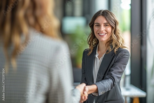 Happy mid aged business woman manager handshaking greeting client in office. Smiling female executive making successful deal with partner shaking hand at work standing at meeting table