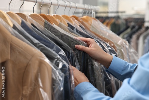 Dry-cleaning service. Woman taking jacket in plastic bag from rack indoors, closeup