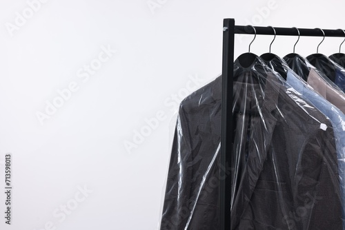 Dry-cleaning service. Many different clothes in plastic bags hanging on rack against white background, space for text