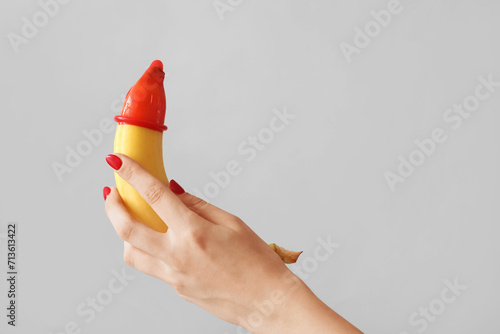 Woman holding banana with condom on light background. Sex concept