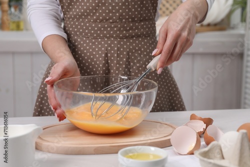 Woman whisking eggs in bowl at table indoors  closeup