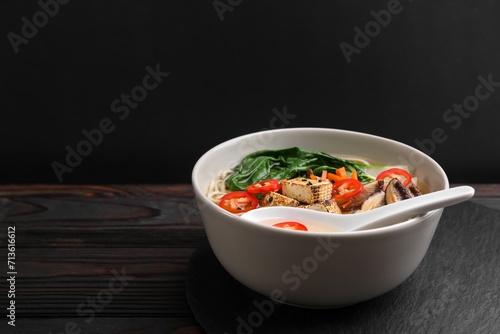 Bowl of vegetarian ramen and spoon on dark wooden table, space for text