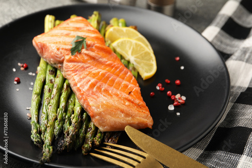 Tasty grilled salmon with asparagus, lemon and spices served on table, closeup