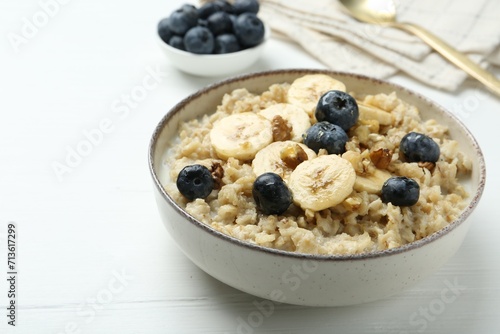 Tasty oatmeal with banana, blueberries, walnuts and honey served in bowl on white wooden table, space for text
