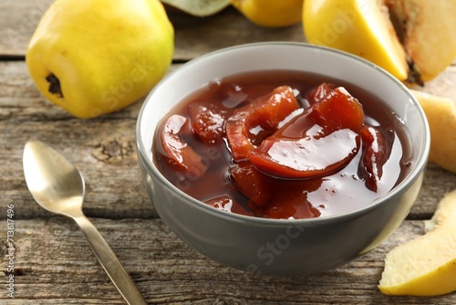Fototapeta Naklejka Na Ścianę i Meble -  Tasty homemade quince jam in bowl, spoon and fruits on wooden table, closeup
