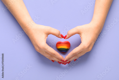 Fototapeta Naklejka Na Ścianę i Meble -  Female hands with heart in colors of LGBT flag on lilac background