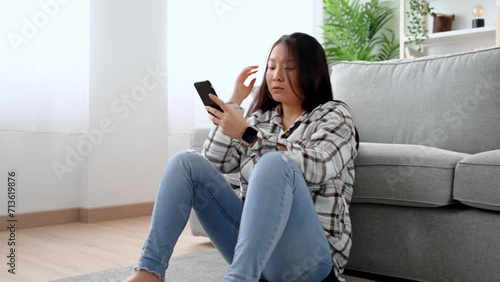 Sad asian woman using phone in the living room. Frustrated young person looking at social media.
