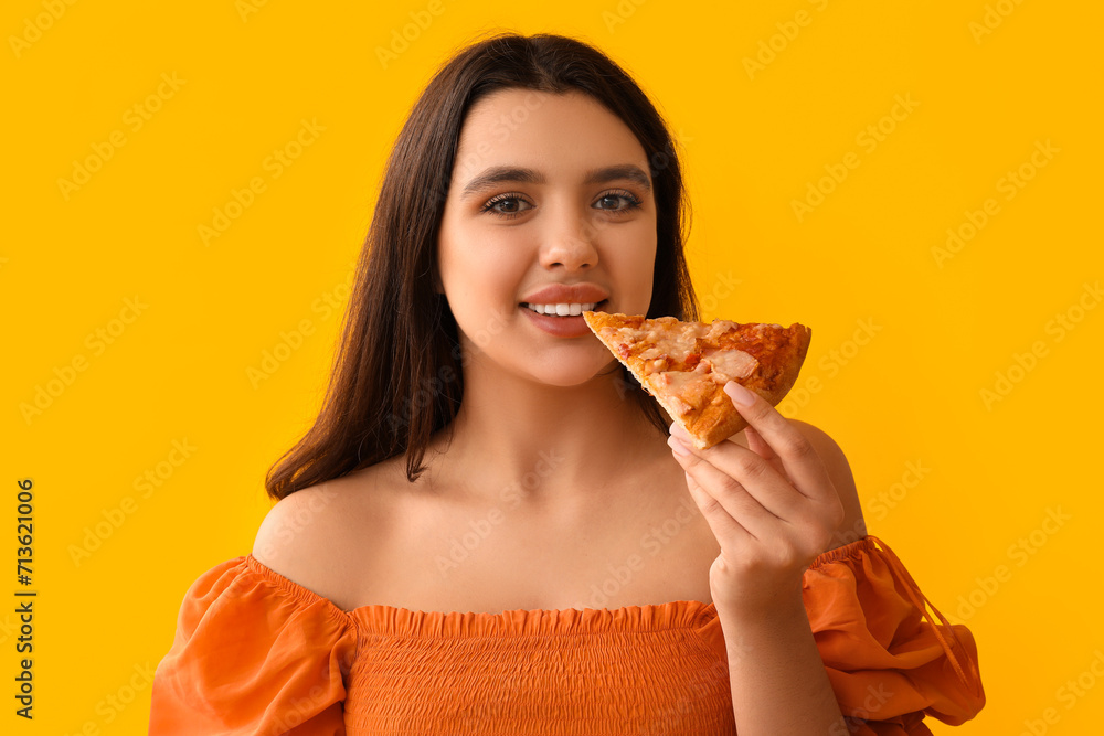 Young woman eating piece of tasty pizza on yellow background Young woman eating piece of tasty pizza on yellow background