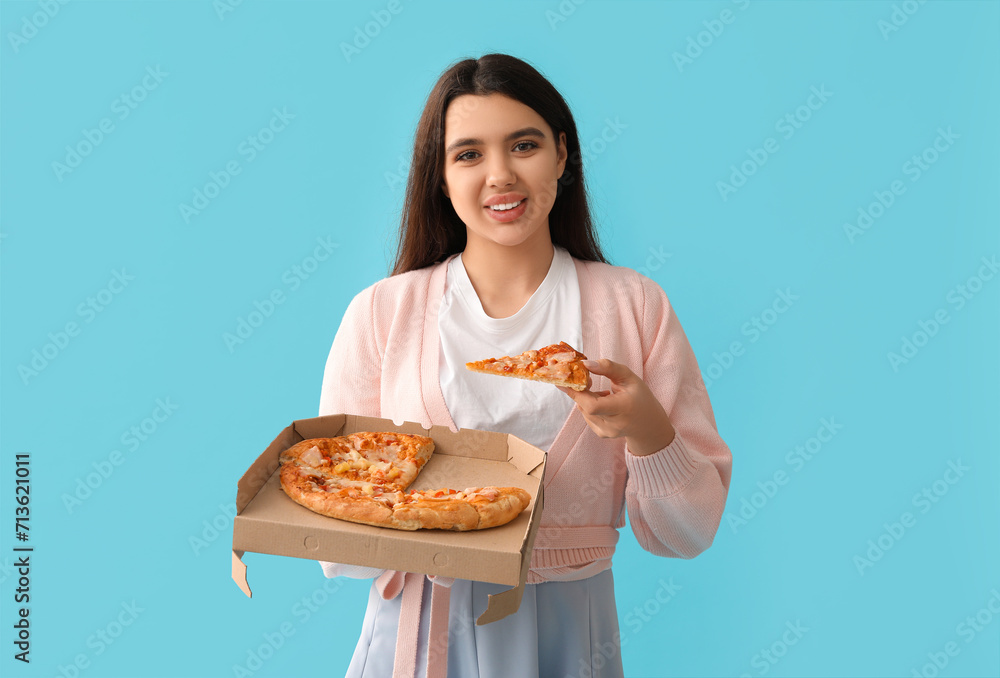 Young woman holding cardboard box with tasty pizza on blue background