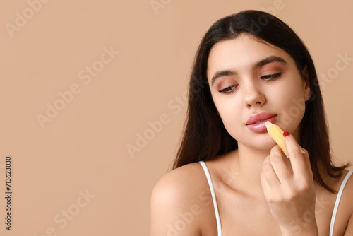 Beautiful young woman applying lip balm on color background