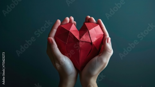 Two female hands holding red polygonal paper heart shape