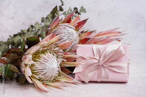Beautiful pink protea flowers and gift box on light background, closeup