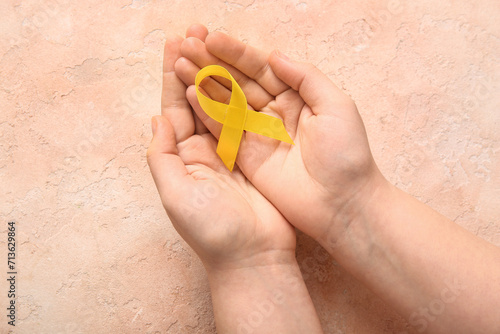 Hands with golden ribbon on beige grunge background. Children cancer awareness concept