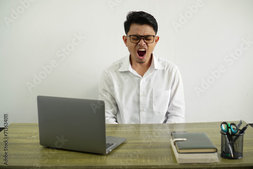 young asian businessman in a workplace shouting to the front with mouth wide open wear white shirt with glasses isolated
