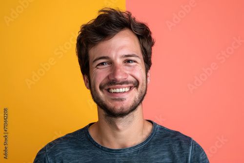 A man with a beard is smiling in front of a pink and yellow background