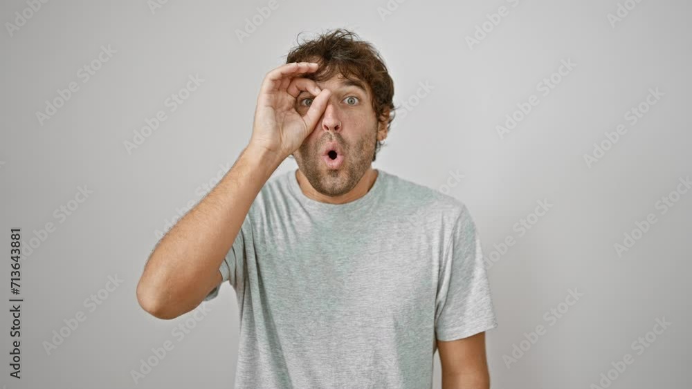 Surprised young man in t-shirt gives ok sign, peeping through fingers in shock. eyes wide open with disbelief over white isolated background. Surprised young man in t-shirt gives ok sign, peeping through fingers in shock. eyes wide open with disbelief over white isolated background.
