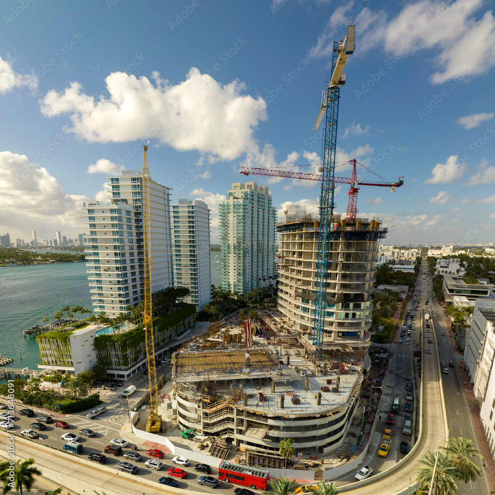 Obraz premium Tower lifting cranes at high residential apartment building construction site. Real estate development in Miami urban area
