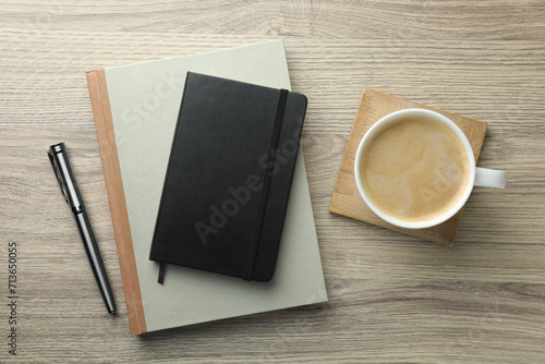 Different notebooks, pen and cup of coffee on wooden table, flat lay